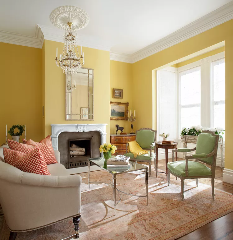 A yellow living room with sage green upholstered chairs, a cream colored sofa and plenty of sunlight.