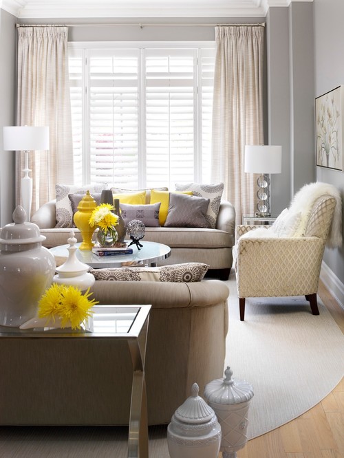 A gray and yellow living room with yellow throw pillows, a yellow urn and yellow mums. The sofas are light gray and the carpet is also gray.