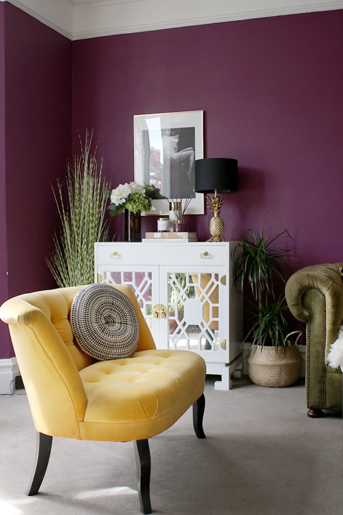 A living room with dark plum walls and yellow upholstery.