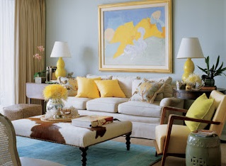 A blue and yellow living room with light blue walls and yellow accessories including yellow lamps, pillows, chair upholstery and flowers.