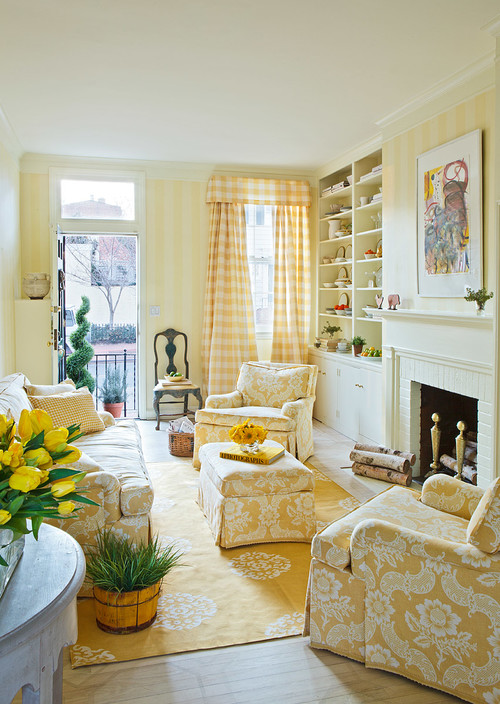 A sunny yellow living room with a yellow rug with white medallions, yellow and white damask upholstery, yellow and white striped wallpaper and checked curtains. There is an arrangement of yellow tulips in the foreground.