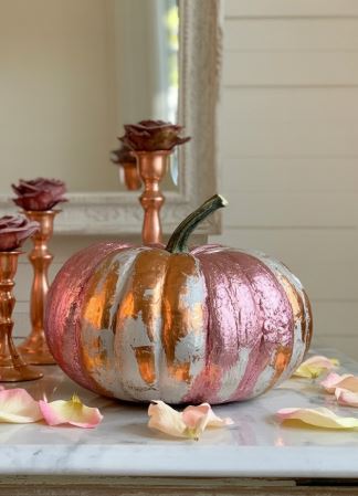 A modern fall decor display featuring a metallic pink and copper pumpkin